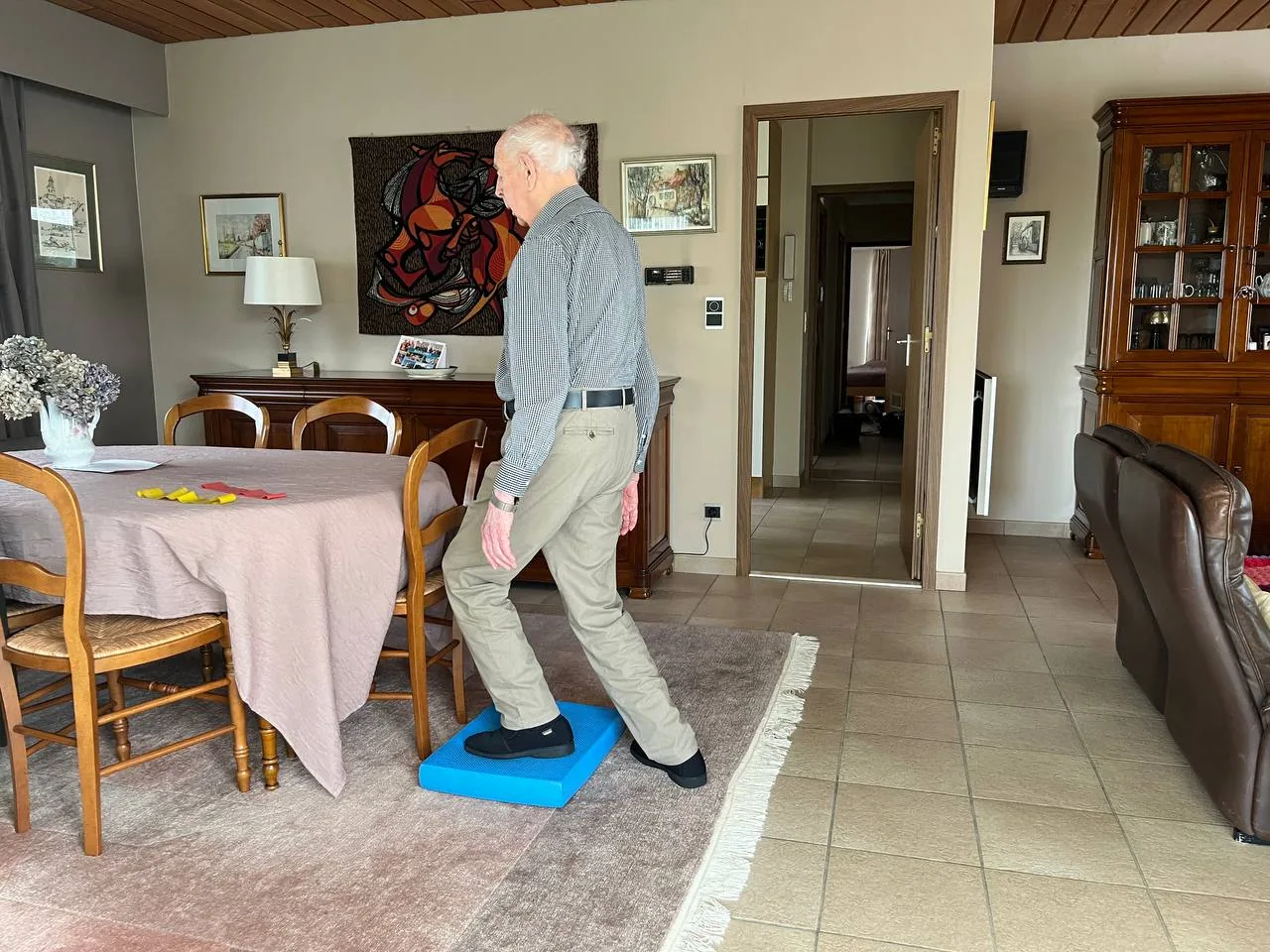 Oudere man oefent thuis in de woonkamer zijn evenwicht door met één voet op een instabiel balanskussen te stappen